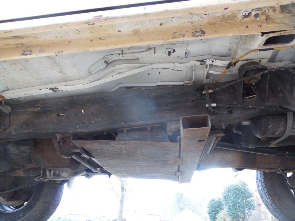 Underside of a truck showing rusty frame rails, crossmember and fuel tank