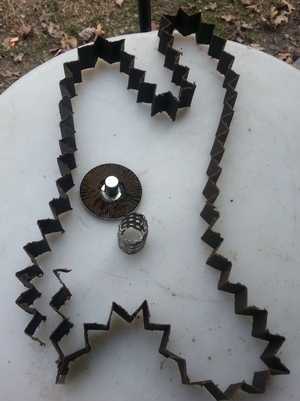 Unfolded dirty pleated filter media, rusty end cap, and perforated metal tube from a disassembled filter on a white table