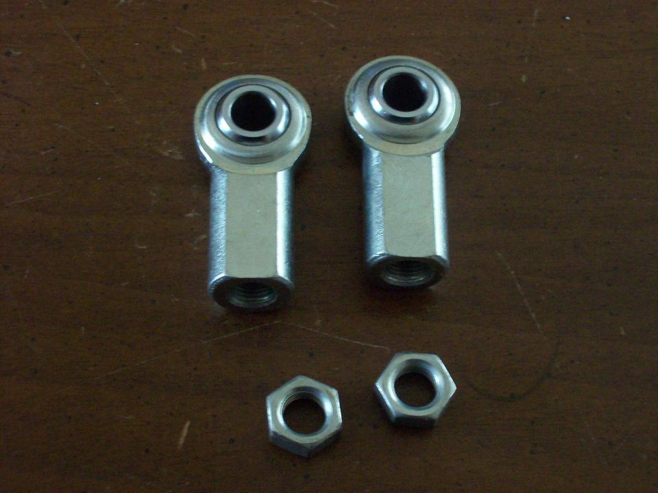 Two metal rod end bearings with threaded ends and two hex nuts on a wooden surface
