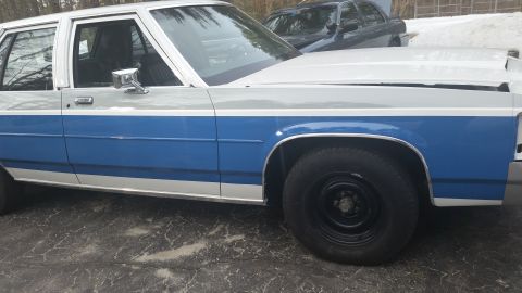 1991 Ford LTD Crown Victoria - A two-tone white and blue sedan is parked outdoors, with another vehicle visible in the background.