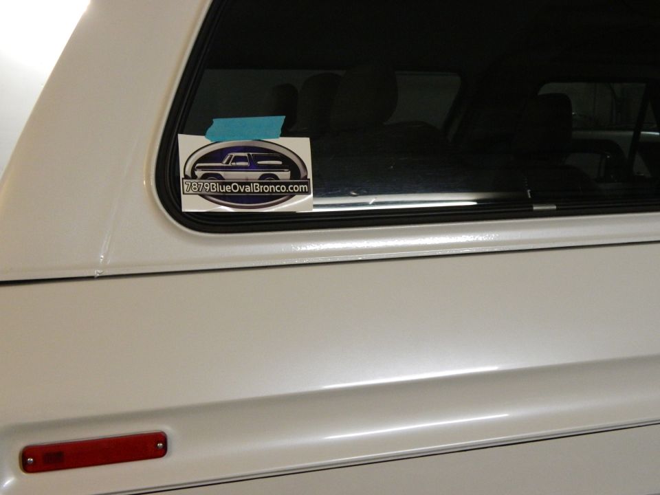 White vehicle with a sticker showing a 1979 Ford Bronco and "7979BlueOvalBronco.com"