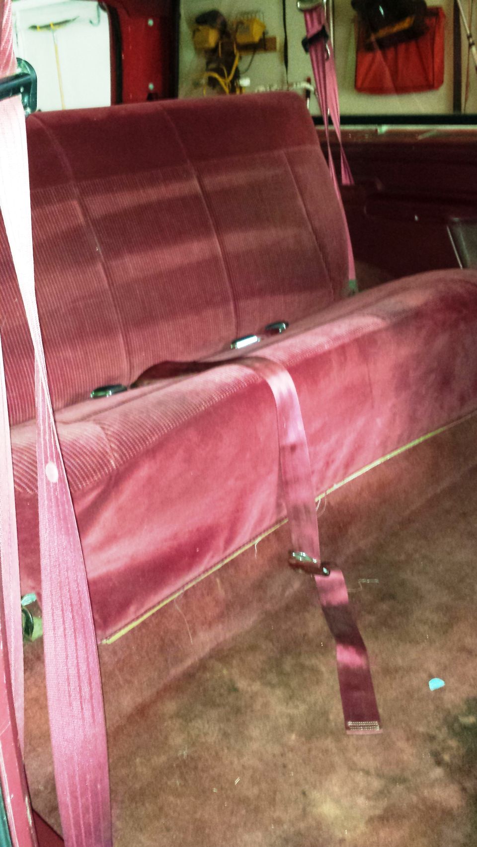 Maroon velour bench seat with pink seatbelts, viewed from the side