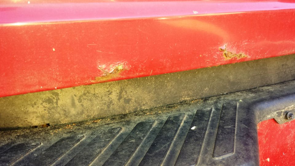 Red truck bed corner with rust and black plastic trim