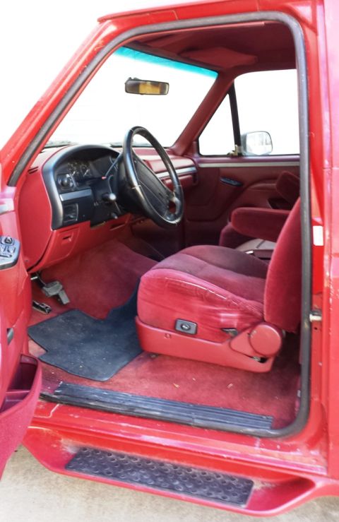 2001 Ford F-150 - Interior of a red truck, likely from the mid-1990s, with velour seats and a black floor mat.