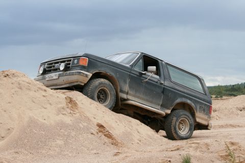 1987 Ford Bronco - 1987 Ford Bronco navigating off-road terrain on a sand dune under a cloudy sky.