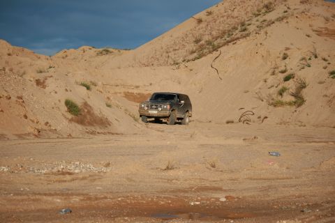 1987 Ford Bronco - A 1987 Ford Bronco navigates a sandy, hilly terrain under a blue sky.