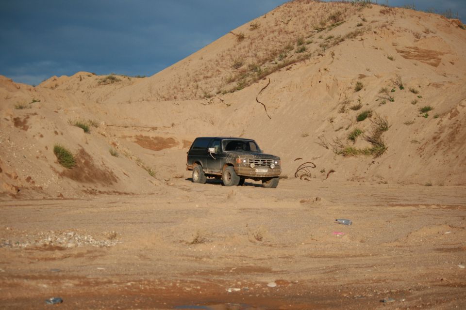 1987 Ford Bronco parked in a sandy area with hills in the background