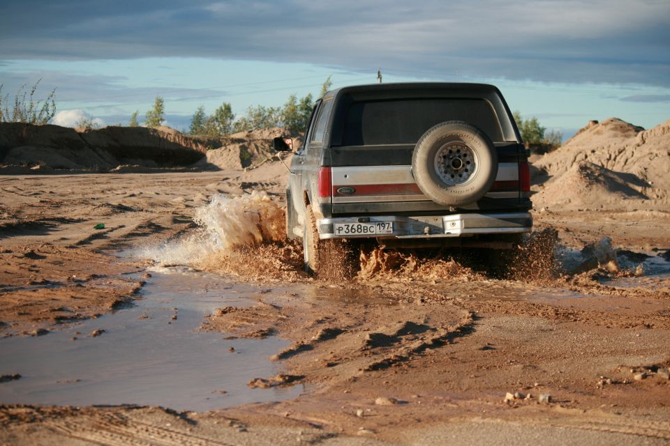 1987 Ford Bronco driving through mud, spare tire mounted on rear door
