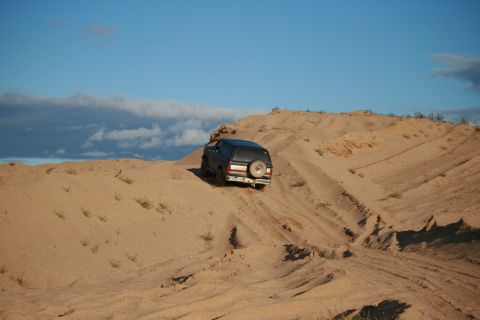 1987 Ford Bronco - SUV navigates sandy terrain under a partly cloudy sky.