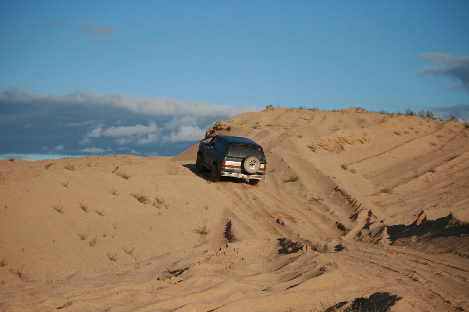 1987 Ford Bronco driving up a sand dune, spare tire visible on rear door