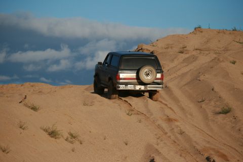 1987 Ford Bronco - This 1987 Ford Bronco is navigating a sandy terrain under a partly cloudy sky.