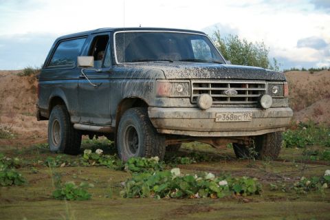 1987 Ford Bronco - Mud-covered 1987 Ford Bronco sits off-road, showing its grille and front end.