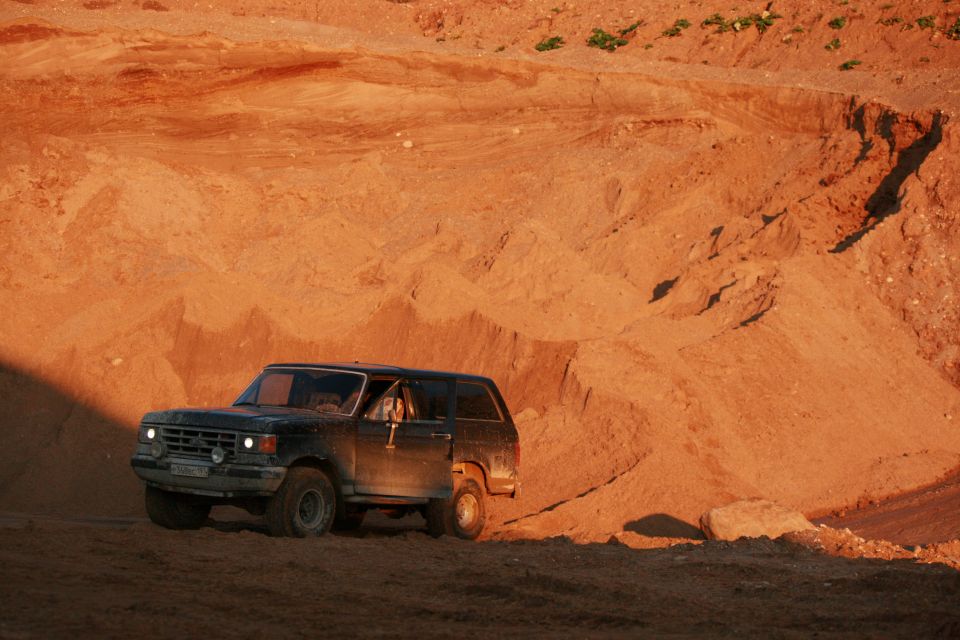 1987 Ford Bronco driving on a sandy hill, driver visible through window