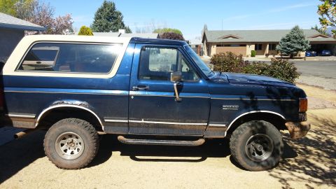 1990 Ford Bronco - This blue Ford Bronco is parked outside a suburban house on a sunny day.