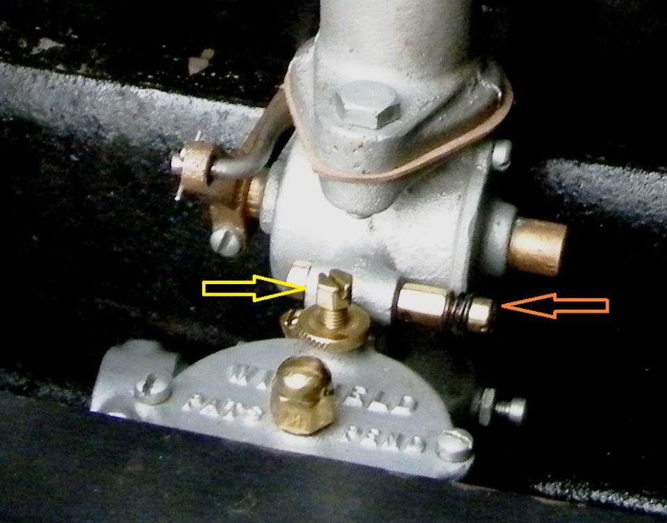 Carburetor assembly with brass fittings and adjustment screws, indicated by yellow and orange arrows