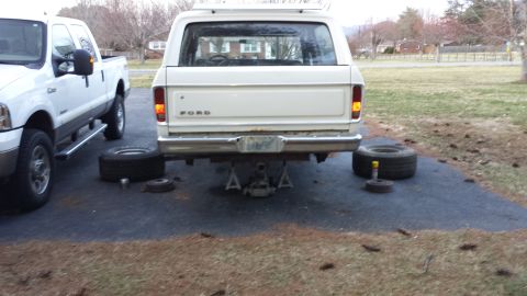 1978 Ford Bronco - Rear view of a white 1978 Ford Bronco being worked on, with a pickup truck nearby.