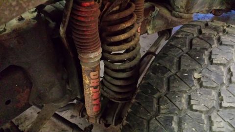 1978 Ford Bronco - Close-up of a vehicle's front suspension, showing a coil spring and a red shock absorber with visible text.