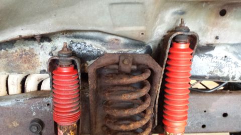 1978 Ford Bronco - Close-up of the undercarriage showing suspension components, including red shock absorbers and rusty coil springs.