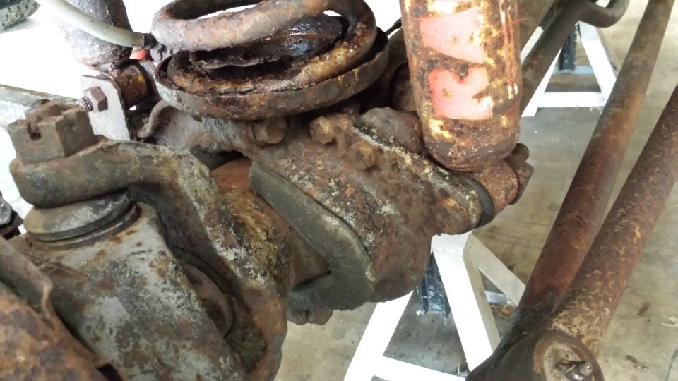 Close-up of heavily rusted suspension components, including a coil spring and ball joint assembly, resting on white jack stands