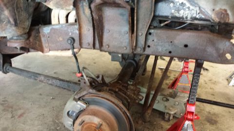 1978 Ford Bronco - The underside of a heavily rusted vehicle is shown, with the suspension system and frame components exposed.