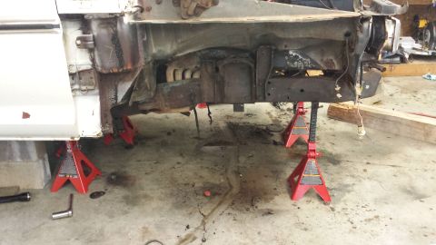 1978 Ford Bronco - Front frame of a 1978 Ford Bronco is elevated on red jack stands in a garage.
