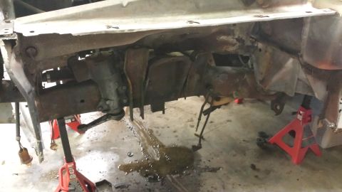1978 Ford Bronco - The underside of a vehicle is shown, supported by jack stands, revealing its frame and suspension system.