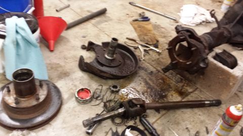 1978 Ford Bronco - Various vehicle parts, including a hub, rotor, and axle components, are laid out on a workshop floor.