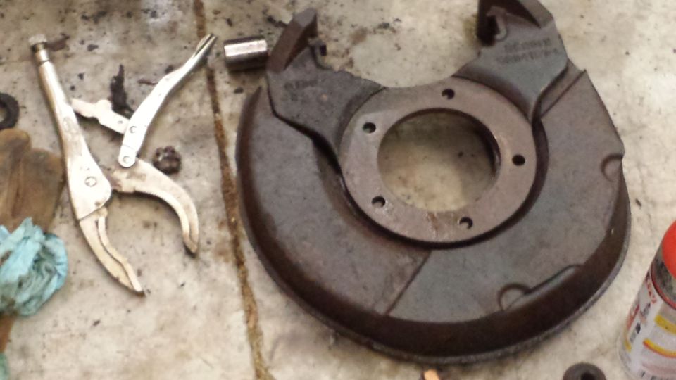 Rusty brake dust shield with vise grips and a socket on a concrete surface