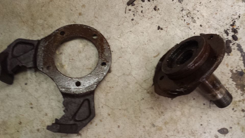 Two rusty metal automotive parts, possibly from a drivetrain, lie on a concrete floor