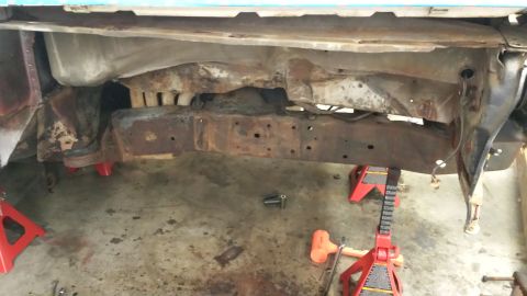 1978 Ford Bronco - The underside of a vehicle, heavily rusted and supported by jack stands in a garage.