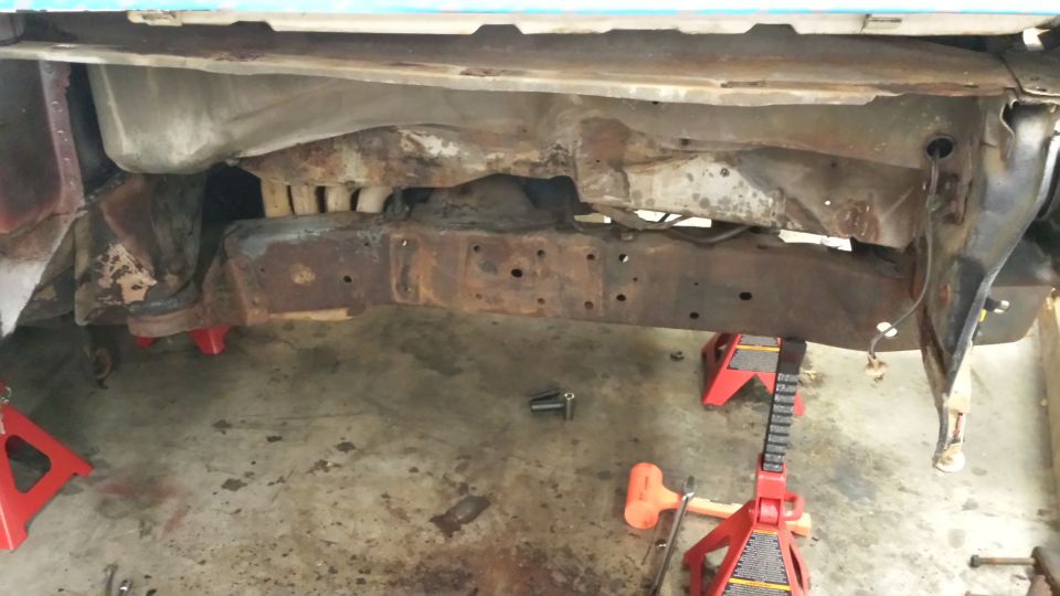rusted frame of a vehicle on red jack stands, showing extensive rust and damage