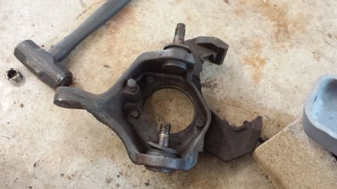 1978 Ford Bronco - A steering knuckle assembly and a hammer are shown on a concrete floor.
