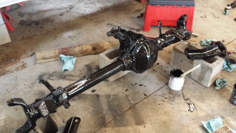 1978 Ford Bronco - A freshly painted rear axle assembly sits on a garage floor with a can of black paint.