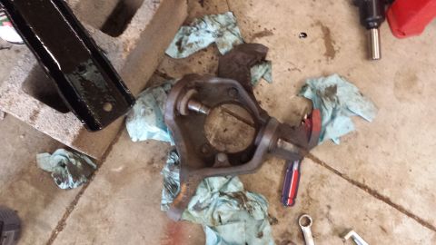 1978 Ford Bronco - A disassembled vehicle spindle assembly lies on a concrete floor, surrounded by oily rags and tools.