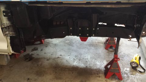 1978 Ford Bronco - The vehicle's frame is elevated on red jack stands, revealing its undercarriage components and suspension.