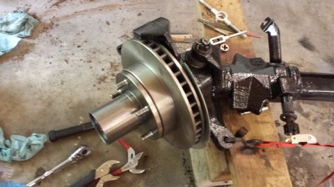 1978 Ford Bronco - A vehicle's front axle assembly, including the brake rotor and suspension components, is shown disassembled on a workshop floor.
