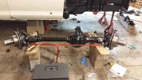 1978 Ford Bronco - Front axle assembly, likely from a truck or SUV, is supported by jack stands and wooden blocks for maintenance.