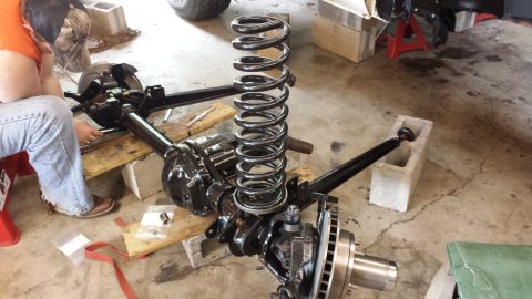1978 Ford Bronco - A person is working on the suspension and axle components of a vehicle, with a large coil spring in the foreground.
