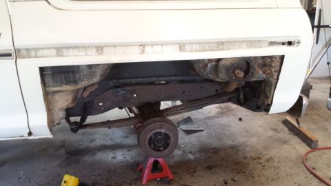 1978 Ford Bronco - The rear suspension and frame of a white Ford Bronco are visible, with the wheel removed and the vehicle supported by jack stands.