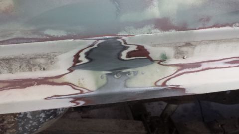 1978 Ford Bronco - Close-up of a car's body panel undergoing repair, revealing layers of filler and primer.