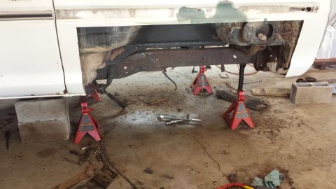 1978 Ford Bronco - The undercarriage of a vehicle is supported by jack stands in a garage, showing rust and repair work.