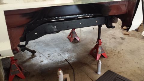 1978 Ford Bronco - Frame of a vehicle is elevated on jack stands, showing underside components during a repair or restoration.