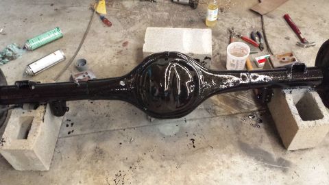 1978 Ford Bronco - A black rear axle assembly rests on cinder blocks, surrounded by tools and spray cans.