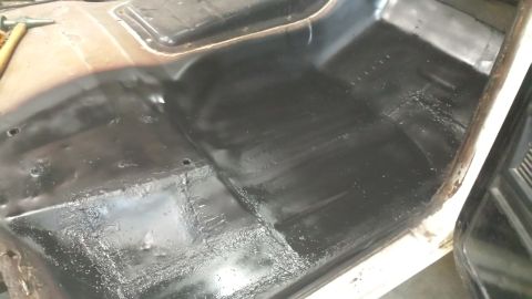 1978 Ford Bronco - The interior floor pan of a vehicle is coated in black, with a hammer nearby.
