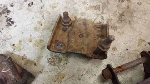 1978 Ford Bronco - A close-up view of a heavily rusted metal bracket with bolts, likely a vehicle part.