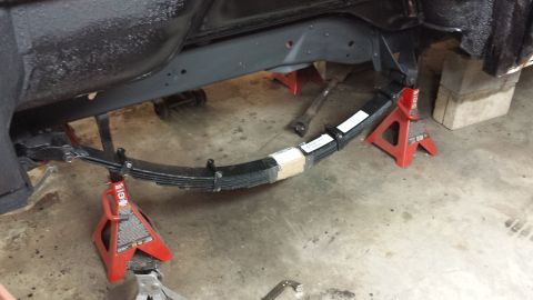 1978 Ford Bronco - The underside of a vehicle is shown, with the leaf spring assembly being worked on and supported by jack stands.