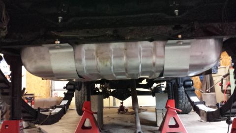 1978 Ford Bronco - The vehicle's undercarriage is visible, with a large fuel tank secured by metal straps.