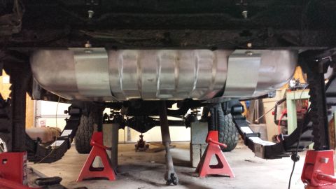 1978 Ford Bronco - The underside of a vehicle is elevated on red jack stands, revealing its fuel tank and suspension components.