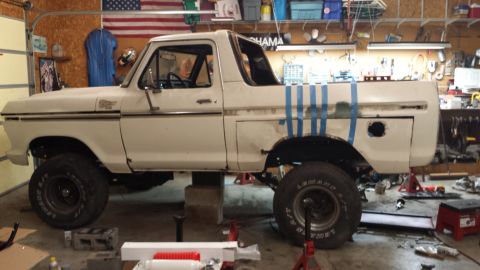 1978 Ford Bronco - A white 1978 Ford Bronco is elevated on jack stands in a garage, undergoing repairs.
