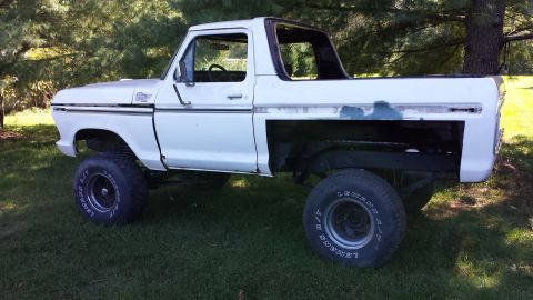 1978 Ford Bronco - White 1978 Ford Bronco with aftermarket wheels and a missing rear quarter panel sits on grass.